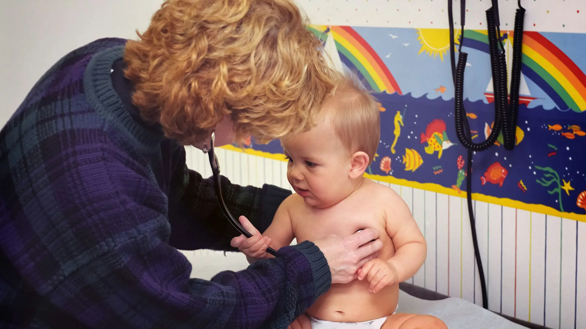 A pediatrician listens to a happy baby's heart in a colorful exam room